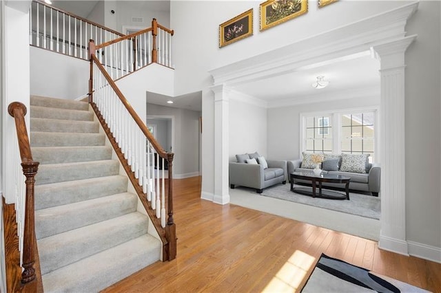 interior space with decorative columns, hardwood / wood-style floors, a towering ceiling, and ornamental molding