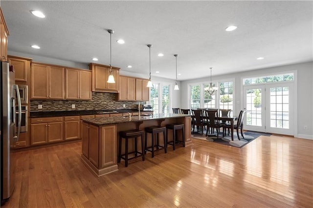 kitchen with dark stone counters, hardwood / wood-style flooring, stainless steel fridge, an island with sink, and decorative light fixtures