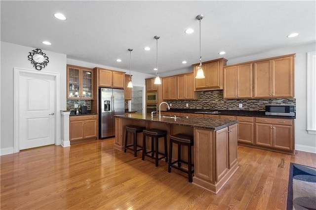 kitchen with pendant lighting, backsplash, light hardwood / wood-style flooring, an island with sink, and appliances with stainless steel finishes