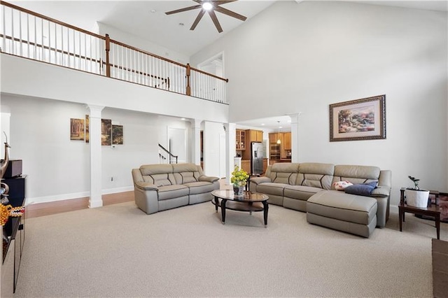 carpeted living room featuring decorative columns, ceiling fan, and high vaulted ceiling