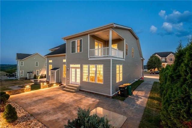 back house at dusk featuring a balcony, a patio, and french doors