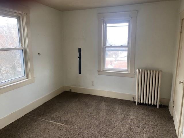 unfurnished room featuring dark carpet and radiator heating unit