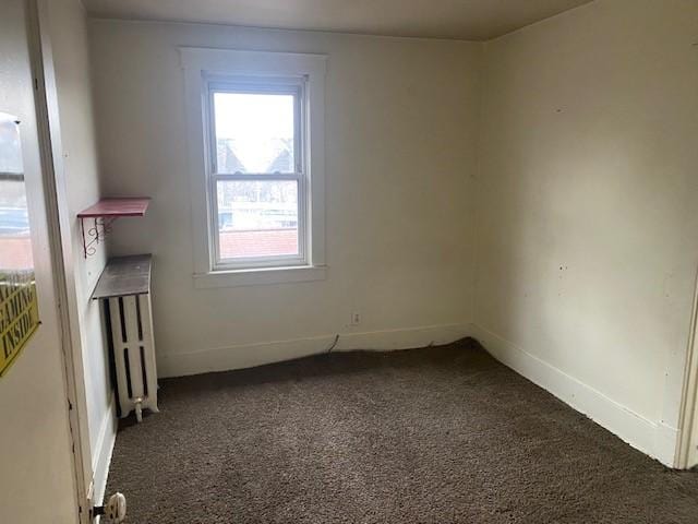 unfurnished room featuring radiator heating unit and dark colored carpet