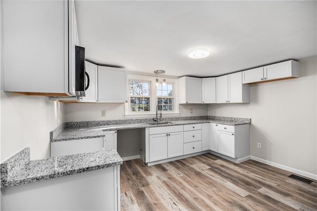 kitchen featuring white cabinets, light stone countertops, wood-type flooring, and sink