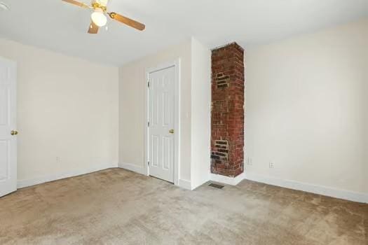 carpeted spare room with ceiling fan and a brick fireplace