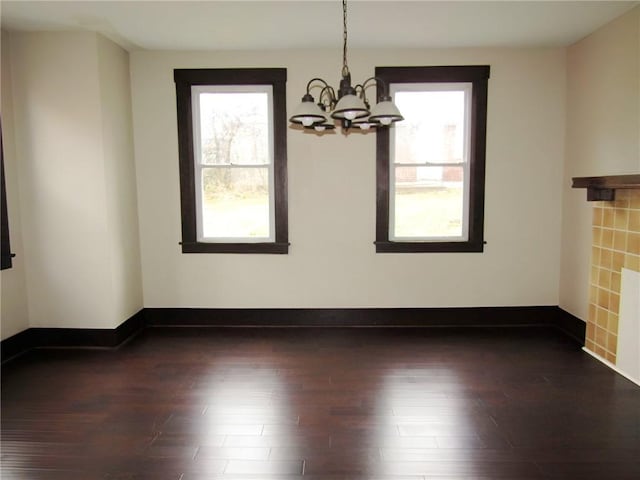 unfurnished dining area with dark wood-type flooring, a healthy amount of sunlight, and an inviting chandelier