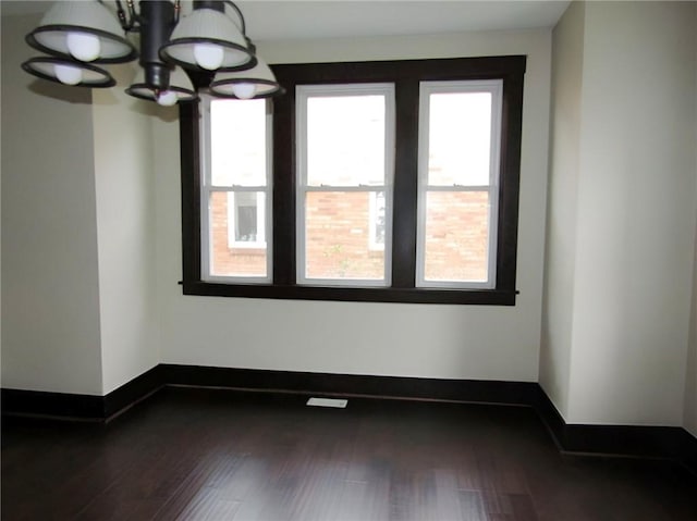 spare room featuring a notable chandelier and dark wood-type flooring