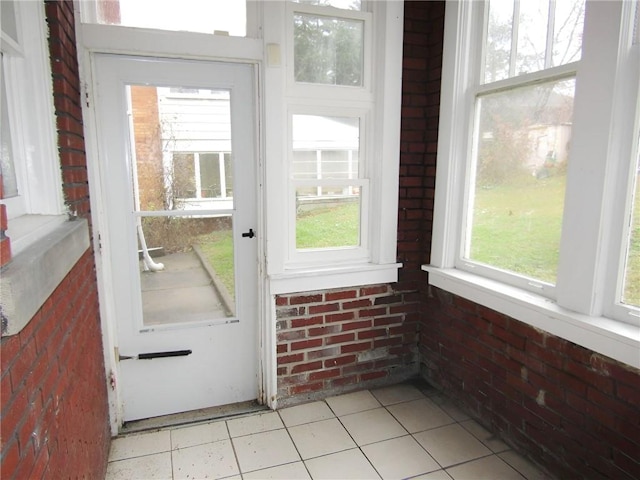 doorway to outside featuring light tile patterned floors, plenty of natural light, and brick wall