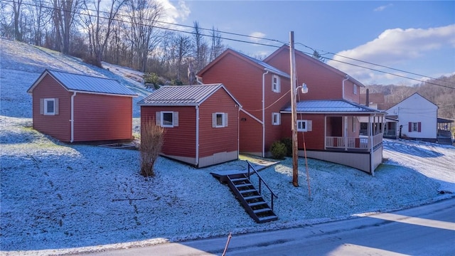 snow covered rear of property with covered porch and an outbuilding