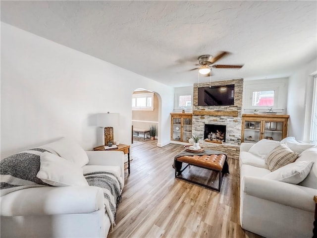 living room with a wealth of natural light, a fireplace, ceiling fan, and light hardwood / wood-style floors