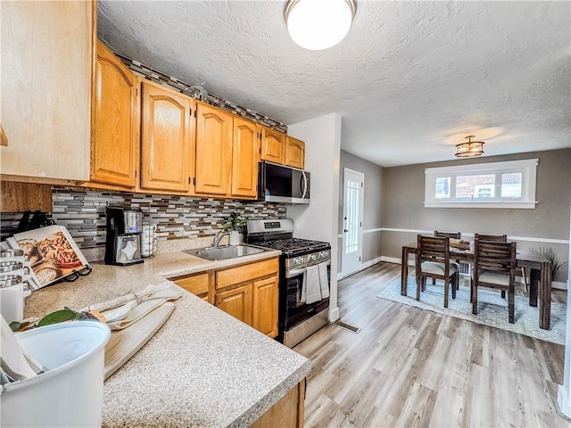 kitchen featuring sink, decorative backsplash, light wood-type flooring, a textured ceiling, and stainless steel appliances