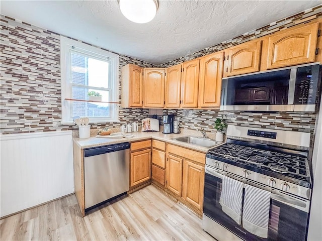 kitchen with backsplash, a textured ceiling, stainless steel appliances, sink, and light hardwood / wood-style floors