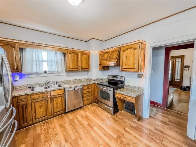 kitchen with light wood-type flooring, premium range hood, light stone counters, stainless steel appliances, and sink