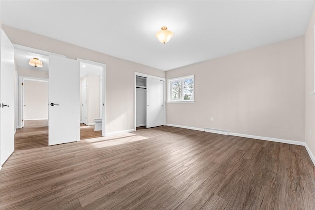 unfurnished bedroom featuring ensuite bathroom, a closet, and hardwood / wood-style flooring