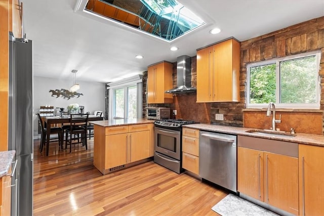 kitchen with sink, light hardwood / wood-style flooring, wall chimney exhaust hood, kitchen peninsula, and stainless steel appliances