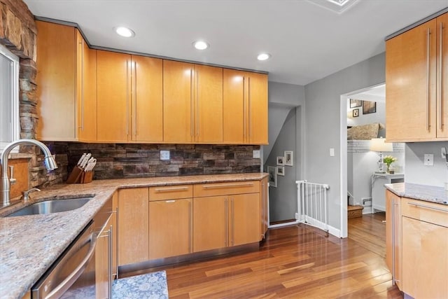 kitchen featuring sink, hardwood / wood-style flooring, stainless steel dishwasher, light stone countertops, and tasteful backsplash