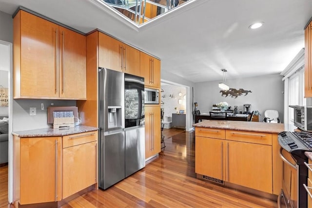 kitchen featuring light hardwood / wood-style flooring, a notable chandelier, kitchen peninsula, pendant lighting, and appliances with stainless steel finishes