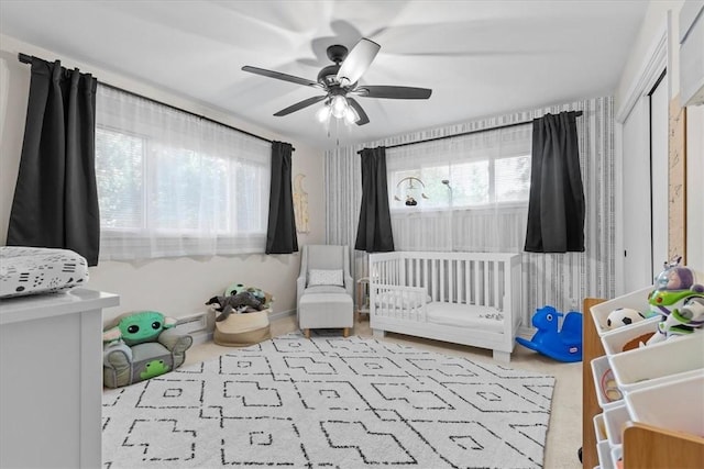 carpeted bedroom featuring a crib and ceiling fan