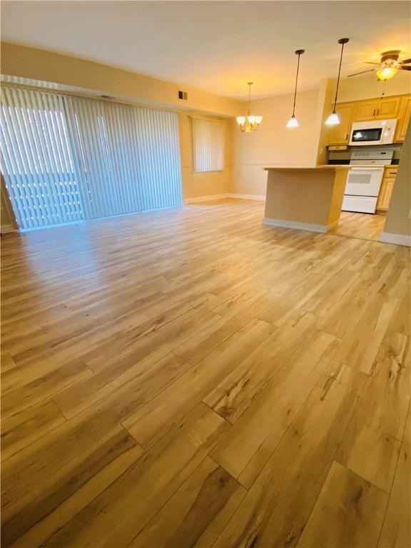 unfurnished living room with ceiling fan with notable chandelier and light hardwood / wood-style flooring