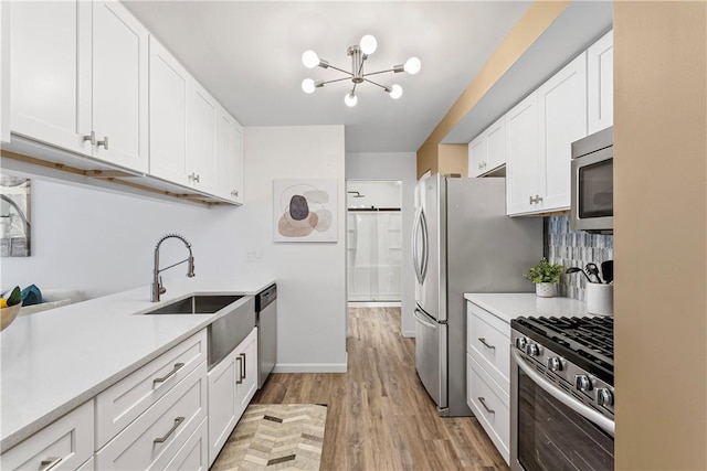 kitchen with appliances with stainless steel finishes, sink, a chandelier, light hardwood / wood-style floors, and white cabinetry