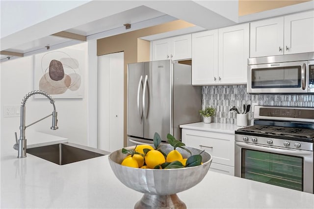 kitchen with tasteful backsplash, sink, white cabinets, and appliances with stainless steel finishes