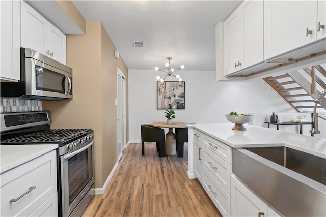 kitchen featuring sink, stainless steel appliances, a chandelier, white cabinets, and light wood-type flooring