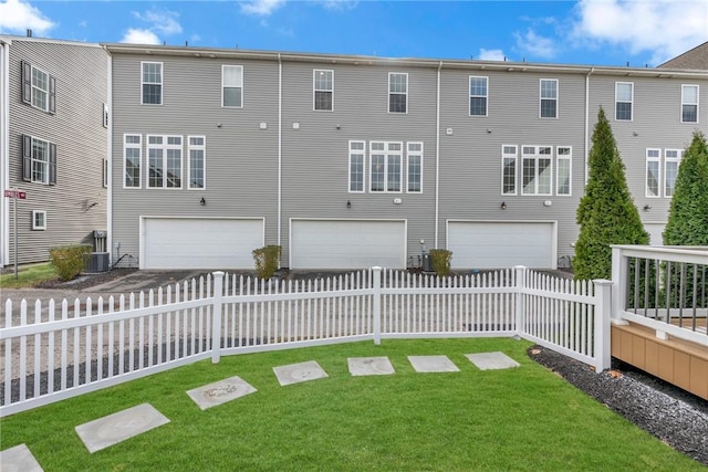 back of property with a yard, central AC unit, and a garage