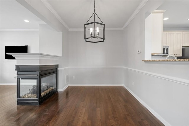 unfurnished dining area featuring a multi sided fireplace, an inviting chandelier, dark hardwood / wood-style floors, and ornamental molding