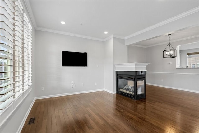 unfurnished living room featuring crown molding, a multi sided fireplace, dark wood-type flooring, and a chandelier