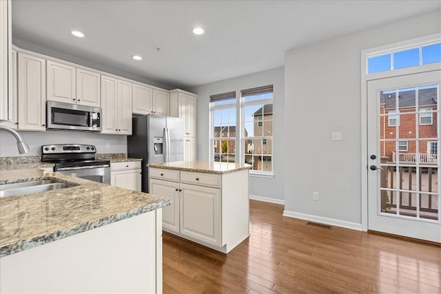 kitchen featuring sink, hardwood / wood-style flooring, appliances with stainless steel finishes, a kitchen island, and white cabinetry