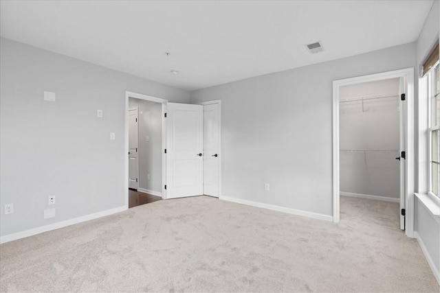 unfurnished bedroom featuring carpet, a walk in closet, and a closet