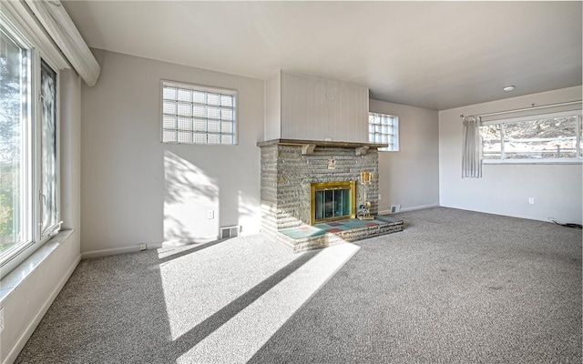 unfurnished living room featuring carpet, a healthy amount of sunlight, and a stone fireplace