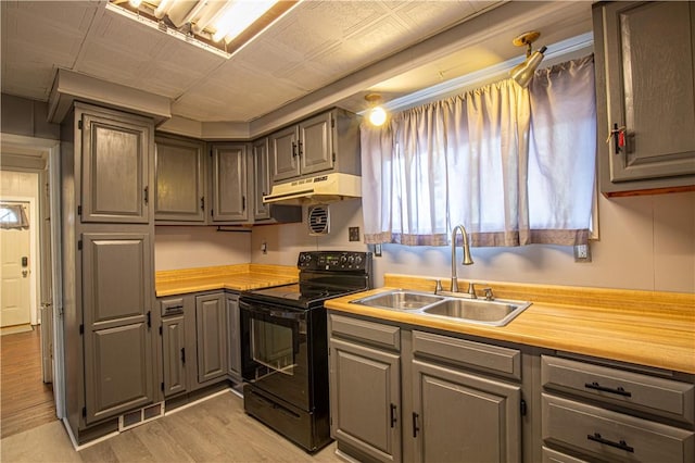 kitchen with light wood-type flooring, butcher block countertops, black electric range oven, and sink