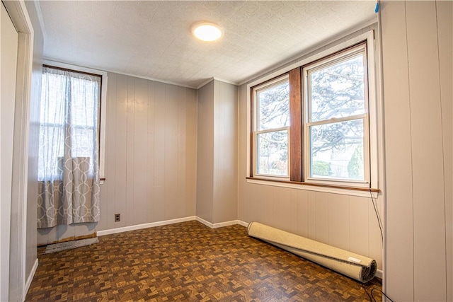 spare room featuring dark parquet flooring, a textured ceiling, baseboard heating, and wooden walls