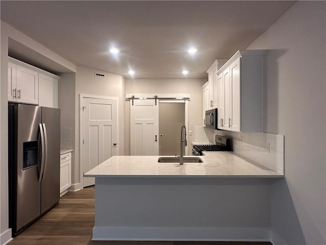 kitchen with appliances with stainless steel finishes, sink, a barn door, white cabinets, and dark hardwood / wood-style floors