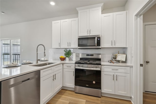 kitchen featuring tasteful backsplash, stainless steel appliances, sink, light hardwood / wood-style flooring, and white cabinetry