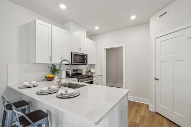 kitchen featuring white cabinetry, a kitchen bar, kitchen peninsula, and appliances with stainless steel finishes