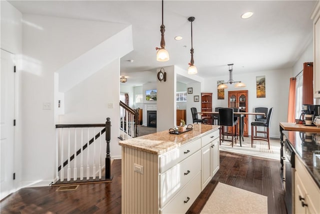 kitchen featuring light stone countertops, dishwasher, a center island, hanging light fixtures, and dark wood-type flooring