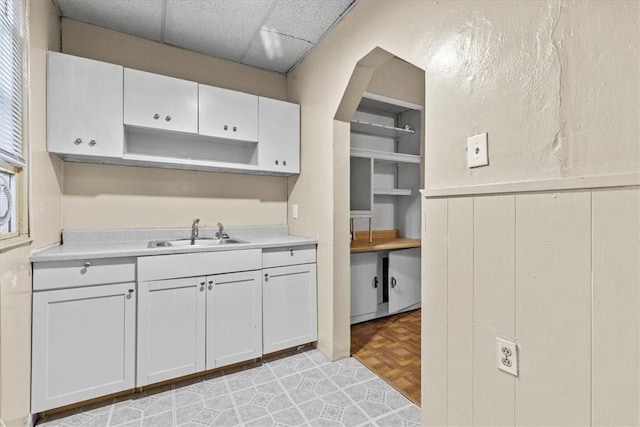 kitchen with white cabinetry, sink, light parquet floors, and a drop ceiling