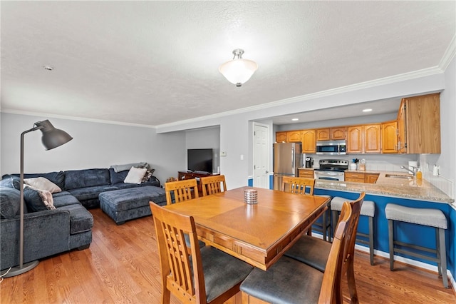 dining room featuring crown molding, sink, a textured ceiling, and light wood-type flooring