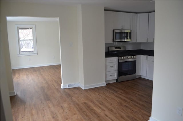 kitchen with decorative backsplash, wood-type flooring, white cabinetry, and stainless steel appliances