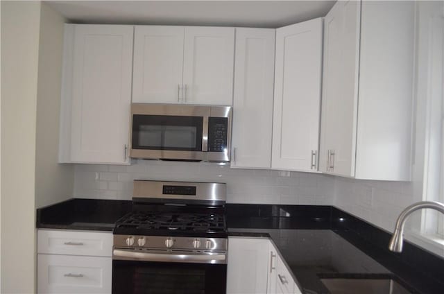 kitchen with appliances with stainless steel finishes, backsplash, dark stone counters, sink, and white cabinetry