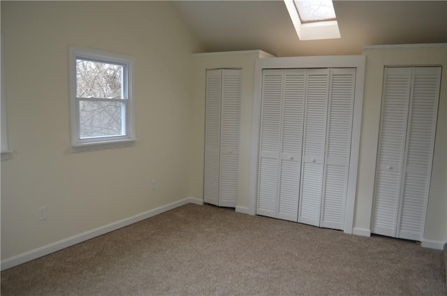 unfurnished bedroom featuring light carpet, multiple closets, and vaulted ceiling with skylight