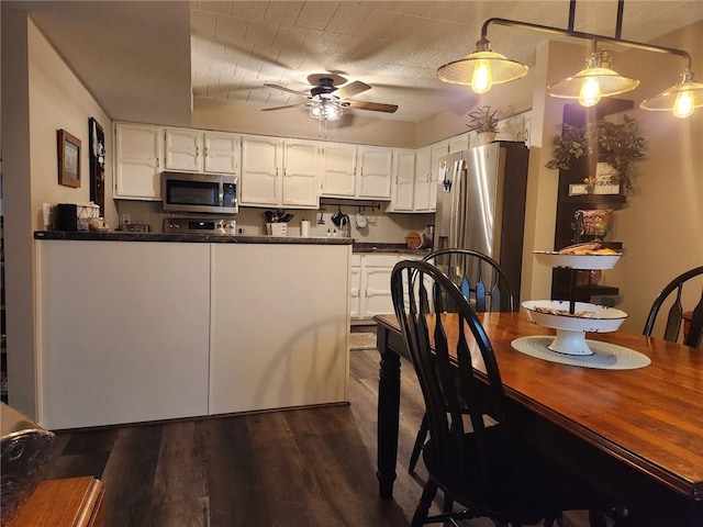 kitchen with appliances with stainless steel finishes, ceiling fan, dark wood-type flooring, white cabinets, and hanging light fixtures