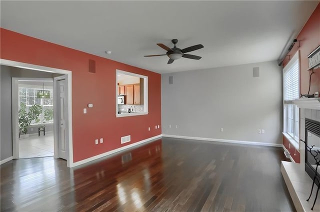 unfurnished living room with sink, dark hardwood / wood-style flooring, ceiling fan, and a tiled fireplace