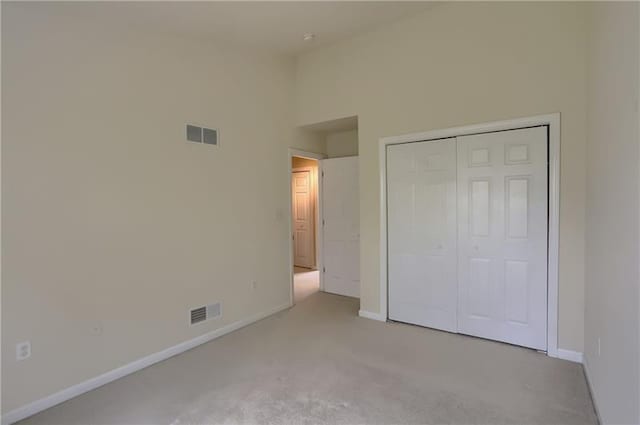 unfurnished bedroom with light colored carpet, a high ceiling, and a closet