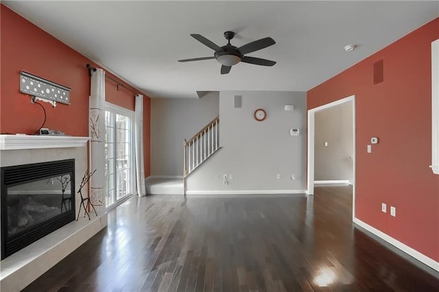 unfurnished living room with a tile fireplace, ceiling fan, and dark wood-type flooring