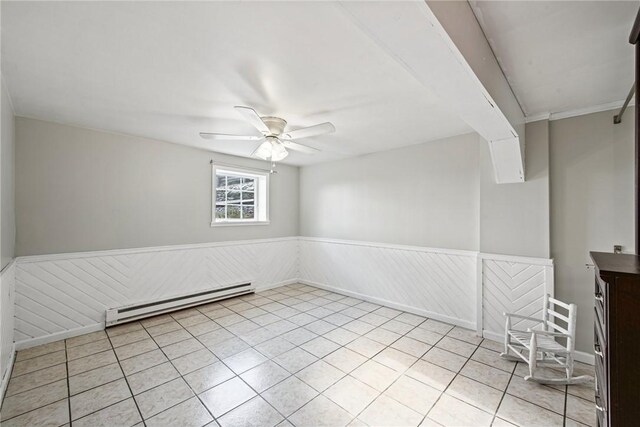 spare room with a ceiling fan, wainscoting, baseboard heating, and light tile patterned flooring