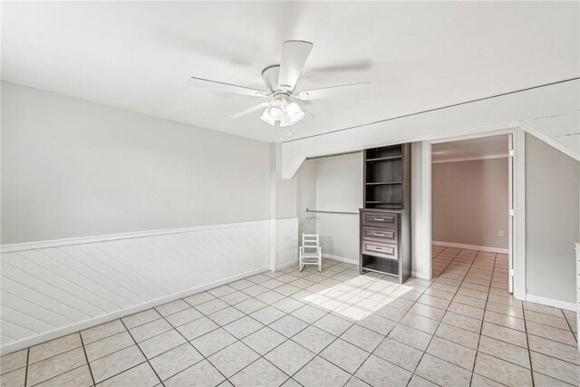 unfurnished bedroom with a closet, a wainscoted wall, ceiling fan, and light tile patterned floors