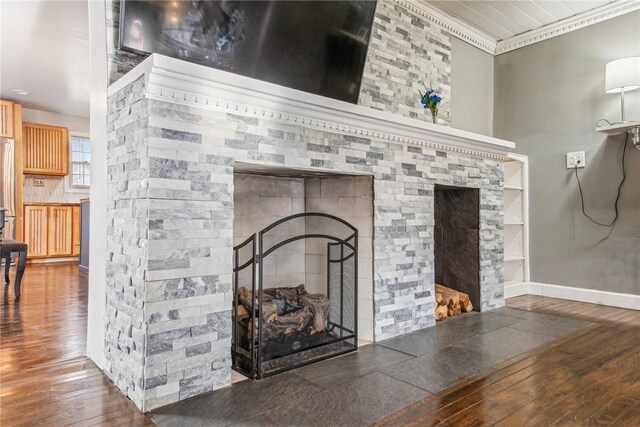 details with ornamental molding, a stone fireplace, wood finished floors, and baseboards